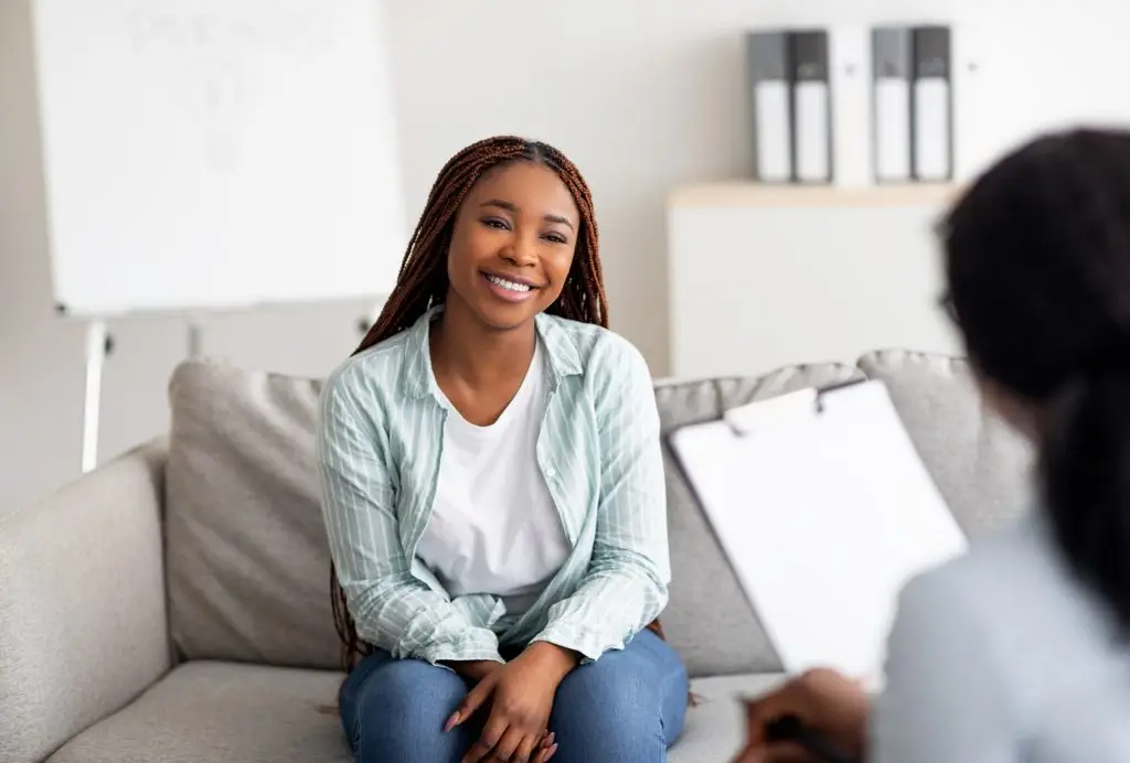Successful therapy. Young female client having consultation with psychologist, grateful for professional help at clinic. Happy black lady speaking with her psychotherapist, solving emotional problem