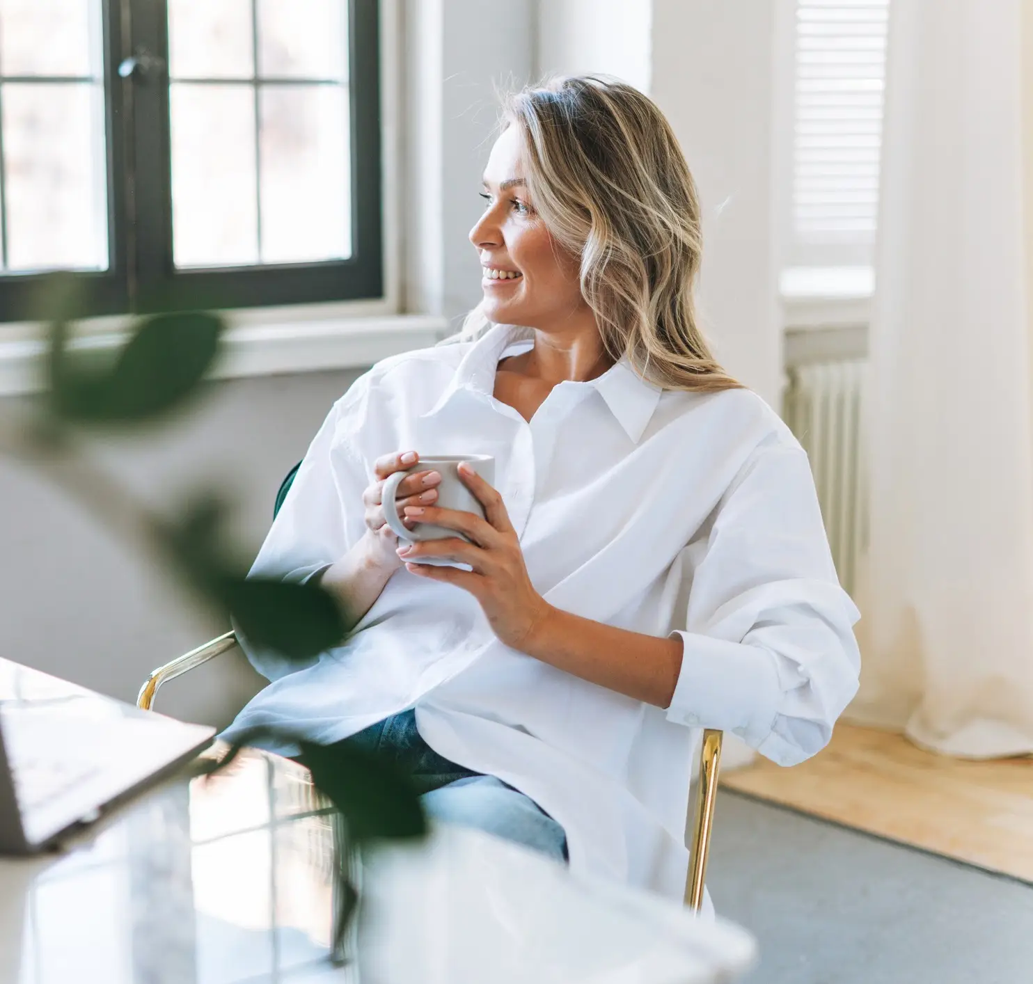 Young smiling blonde woman with long hair in white shirt rest and drinking tea in bright modern office